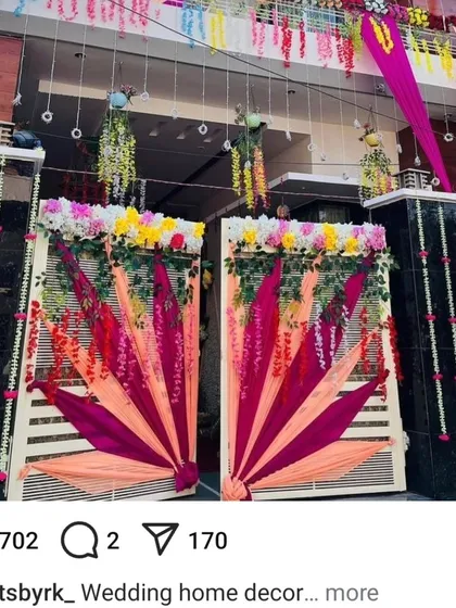 An elaborate and festive main gate decoration for a wedding house. The design uses colorful drapes in a fan-like pattern and is adorned with hanging floral arrangements.