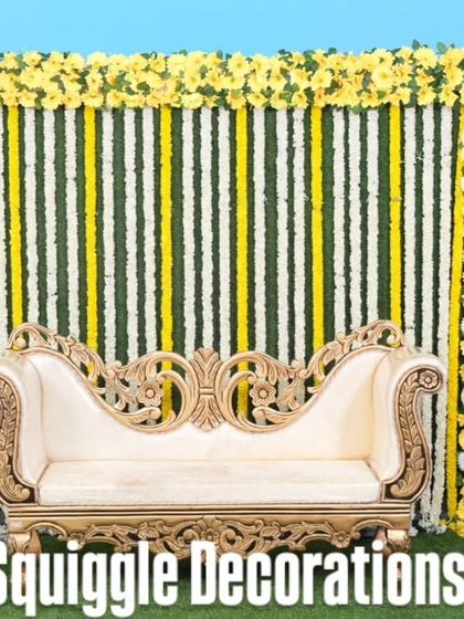 A traditional baby shower photo booth with a backdrop of marigold and tuberose flower strings and an elegant diwan.