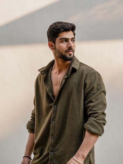 This portrait from a men's lifestyle shoot focuses on a confident, relaxed pose. The simple background and natural light keep the attention on the model's expression and casual style.