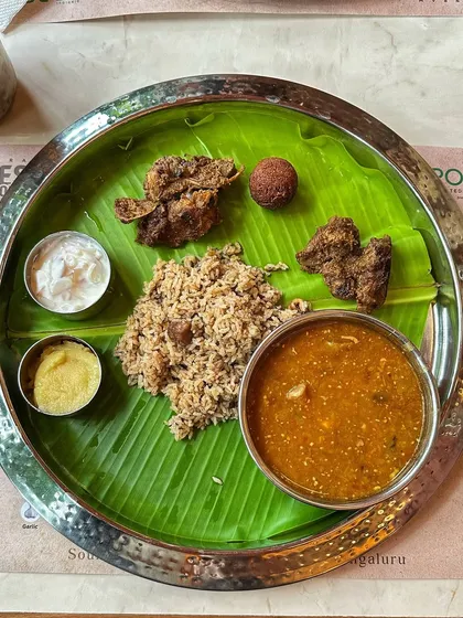A complete Naati style meal served on a banana leaf, featuring mutton palav, fried meat, and various accompaniments. This is a true feast.
