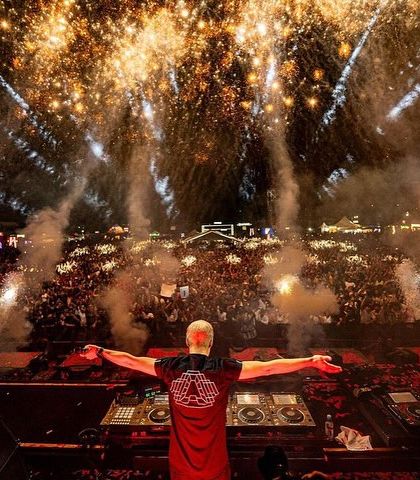 A legendary moment from Armin van Buuren's show. The trance icon stands before a massive crowd with his arms outstretched, surrounded by an explosive fireworks display.