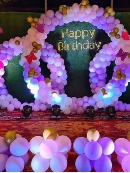An intricate triple-ring balloon backdrop in shades of purple. This unique design with butterfly accents and a neon sign creates a stunning photo opportunity.