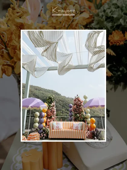 The decor for a colourful Mehendi, featuring a striped sofa, pastel balloon arrangements, and purple umbrellas, all set against a beautiful mountain view.