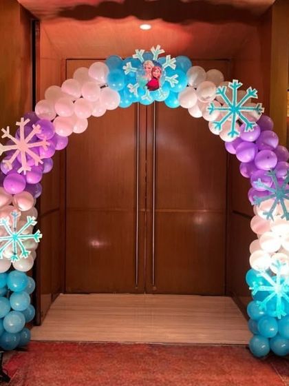 A grand entrance arch for a 'Frozen' party, decorated with balloons and snowflake cutouts, flanked by standees of Anna and Elsa.