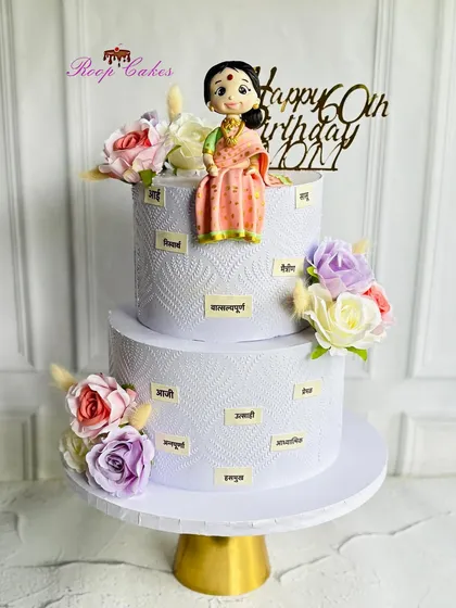 Celebrating 60 graceful years. This two-tier cake is a tribute to a mother, decorated with words in Marathi that describe her wonderful qualities, and topped with a custom fondant figure.