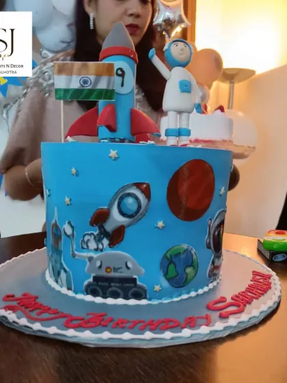 A detailed look at the astronaut-themed cake, featuring a rocket, planets, and an astronaut figure holding the Indian flag.