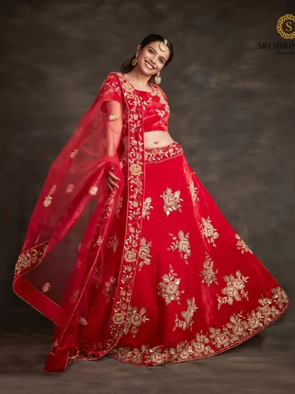 A smiling model twirls in a vibrant red lehenga with gold floral embroidery. This is a classic, joyful look perfect for any bride.