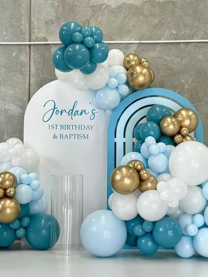 A modern first birthday and baptism setup in shades of blue, white, and gold, with custom arched backdrops and balloon clusters.