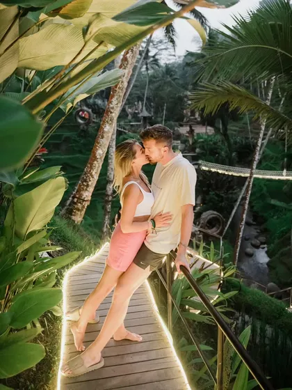 A couple kisses on a beautifully lit wooden walkway amidst the jungle in Bali. This magical setting creates a fairytale-like atmosphere for a romantic pre-wedding photo.