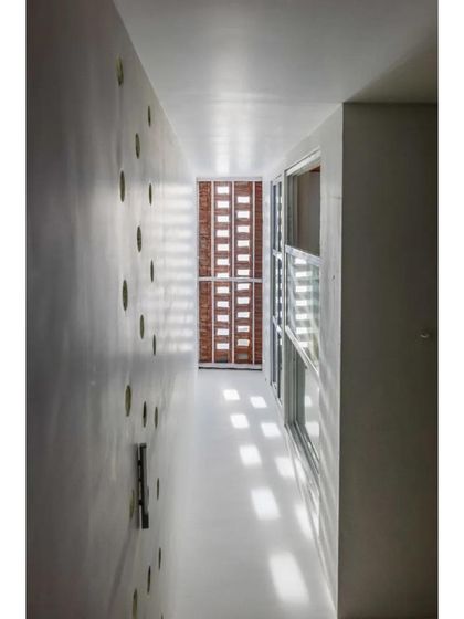 A narrow interior space is illuminated by light filtering through a perforated screen. This project is a masterclass in controlling natural light to create a serene and glare-free environment.