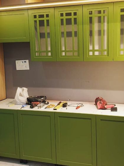A vibrant green storage cabinet under installation in Gurgaon. This piece, designed for a foyer or dining area, features classic shaker-style doors with glass on the upper cabinets for a touch of traditional charm.