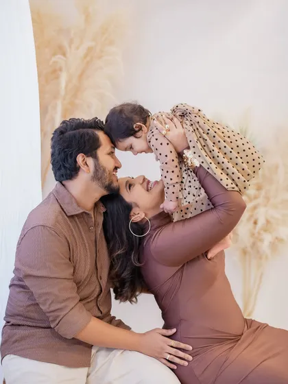 The pure joy of a first birthday. A mother in a beautiful brown dress lifts her smiling baby girl, dressed in a polka-dot frock, high in the air. This candid moment from a family birthday photoshoot is full of laughter and love.