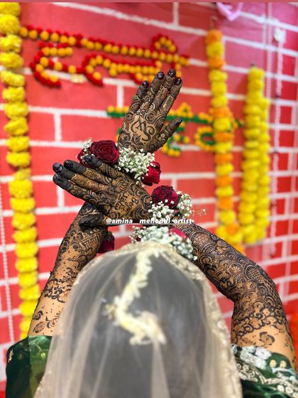 A beautiful shot from behind the bride, showing the full extent of the arm mehendi against a festive backdrop.