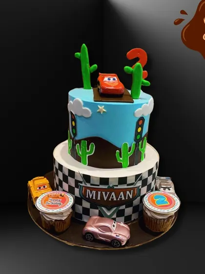This two-tier Disney Cars cake is ready to race. It features a checkered flag base, cactus decorations, and Lightning McQueen on top, along with matching themed cupcakes on the side.