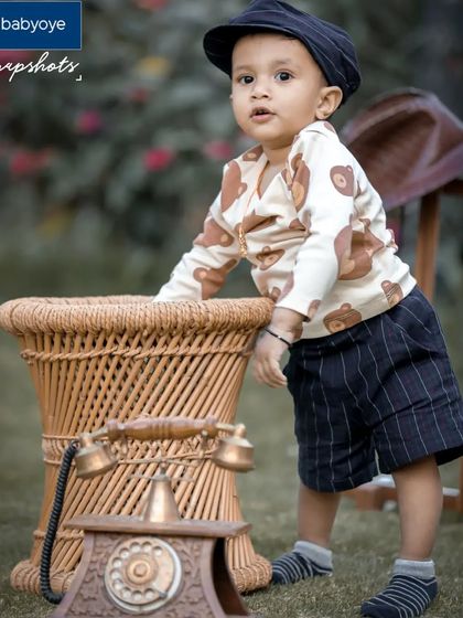 A vintage-themed outdoor shoot featuring classic props like an old-fashioned telephone and wicker furniture. The little boy's outfit perfectly complements the retro vibe.