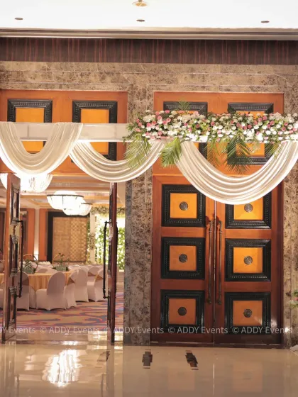 A grand floral entrance to the Nikah ceremony hall. The doorway is framed by an arch of lush flowers and soft, draped fabric, offering a glimpse of the beautiful celebration within.
