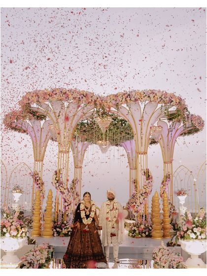 A wide shot of the couple at their magnificent beachside mandap, showered with petals. This image captures the scale and beauty of a destination wedding ceremony.