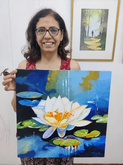 An adult student beams with pride, holding her beautiful acrylic painting of a water lily. It's never too late to pick up a brush and discover a new passion or revisit an old hobby.
