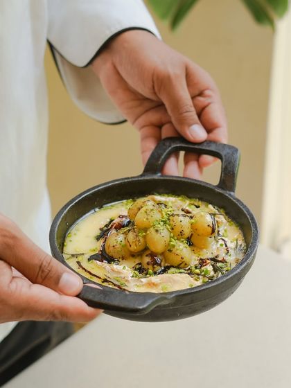 A chef holds our popular melted brie with Kumaoni grapes. This dish is a testament to our philosophy of pairing local artisanal products, like the brie from Spotted Cow, with regional produce.