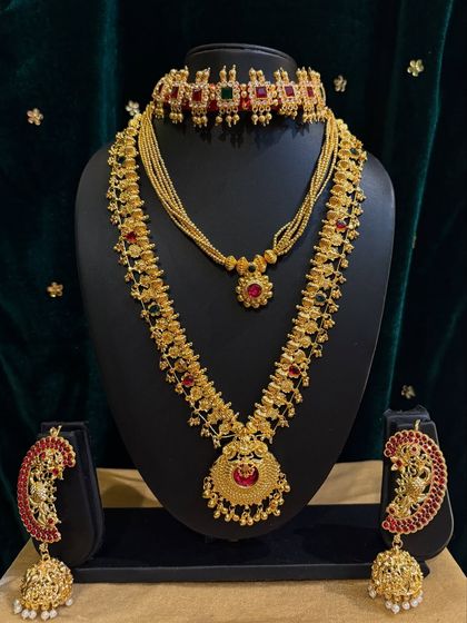 This rental set features a stunning choker and a long haar with peacock-shaped earrings, all studded with red and green stones.