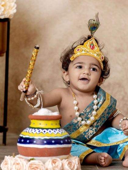 A beautifully composed shot of a baby Krishna with his flute and butter pot, looking off-camera with a sweet, gentle expression.