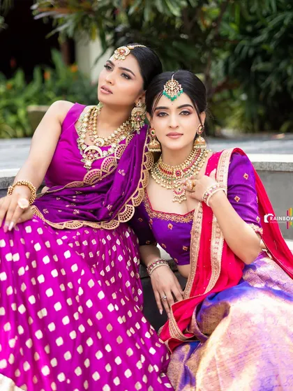 Another angle of the two models, highlighting their regal poses and the rich textures of their lehengas and jewelry.