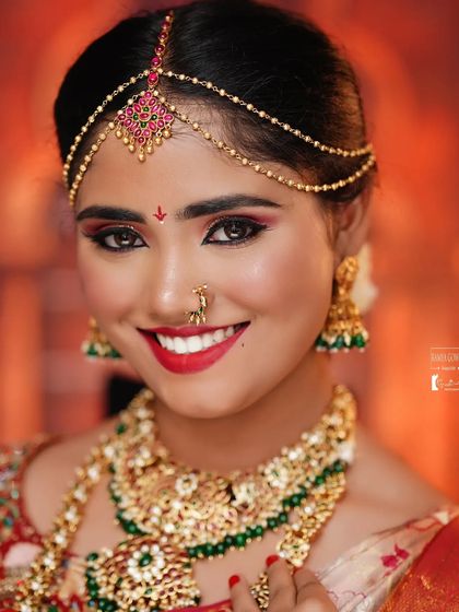 A happy bride smiling for the camera, wearing our grand kundan and green bead bridal set. The matching matha patti and nose ring complete her beautiful look.