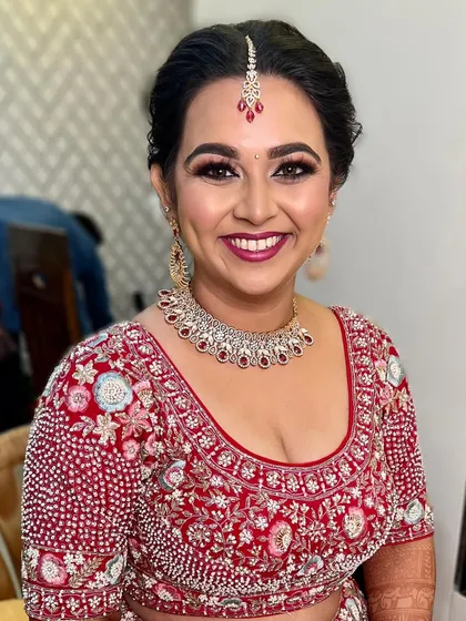 The beautiful smile of a happy bride. Her makeup is classic and radiant, with a bold berry lip that complements her red lehenga perfectly.