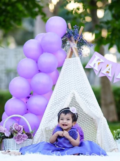 A magical first birthday setup outdoors! Little Kaashvi is celebrating with a purple-themed teepee, balloons, and a custom name banner.