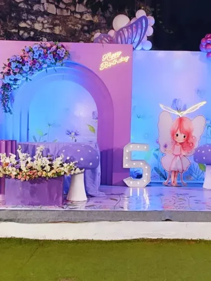 The full view of the enchanting fairy-themed stage, complete with a custom arched backdrop, a fairy cutout, and whimsical mushroom props, all under a canopy of purple and blue balloons.