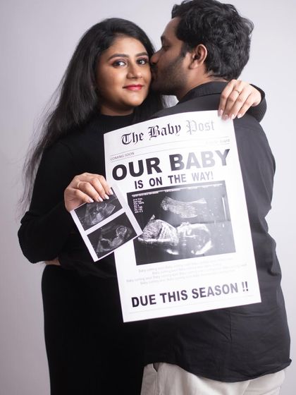 A sweet and intimate announcement photo. The couple holds their ultrasound pictures and a custom newspaper while sharing a happy kiss. It's a perfect blend of props and emotion.