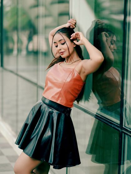 An urban fashion shoot featuring a faux leather top and skirt. The reflection in the glass wall adds a dynamic, modern element to the shot.