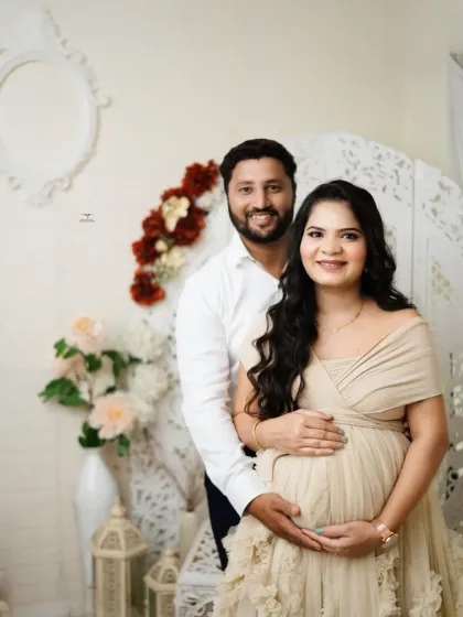 A classic portrait of the expecting couple, smiling warmly at the camera. The neutral tones of their outfits and the bright studio setting make for a fresh and happy photo.