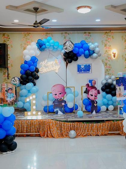A Boss Baby themed stage decoration in a hall. This setup includes a balloon arch, character cutouts, and a light-up number '1' on a decorated stage.