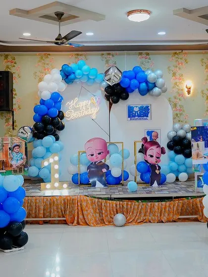 A Boss Baby themed stage decoration in a hall. This setup includes a balloon arch, character cutouts, and a light-up number '1' on a decorated stage.