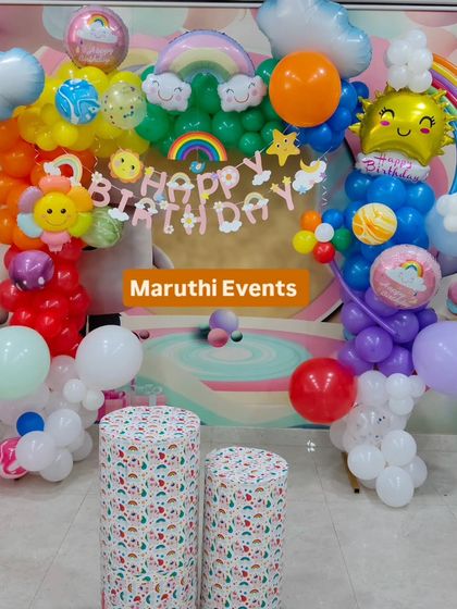 A cheerful rainbow and sunshine theme. This happy setup includes a rainbow balloon arch, smiling sun and cloud balloons, and rainbow-themed plinths.