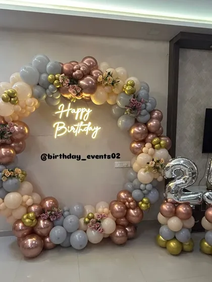 Our signature ring backdrops are a client favorite. This elegant setup features a full circle of pastel, rose gold, and grey balloons, a custom neon sign, and matching balloon stands for the birthday age, creating a polished and trendy photo corner.
