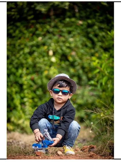 A cool and casual portrait of a young boy in a hat and sunglasses, playing with his toy truck in a natural setting.