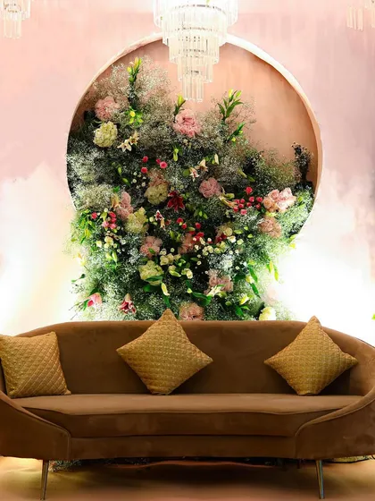 A simple yet elegant stage setup. A modern brown sofa is set against a circular backdrop filled with an explosion of florals and greenery, creating a beautiful focal point for photos.