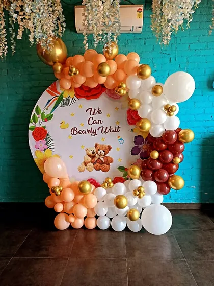 A warm and inviting "We Can Bearly Wait" teddy bear themed baby shower. This setup features a custom backdrop against a teal wall, with a balloon arch in orange, white, and gold.