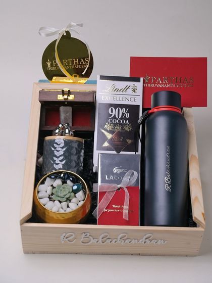 A premium corporate gift hamper I created, featuring a personalized flask, Lindt chocolate, a Lacoste gift, a silver bar, and a succulent plant, all in a custom-engraved wooden box.