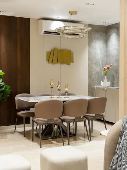 This open-concept dining area is a harmonious blend of texture and tone. From the L-shaped marble cladding to the warm veneer wall, every element plays its part. The sculptural stainless steel artifact anchors the room with statement and soul.