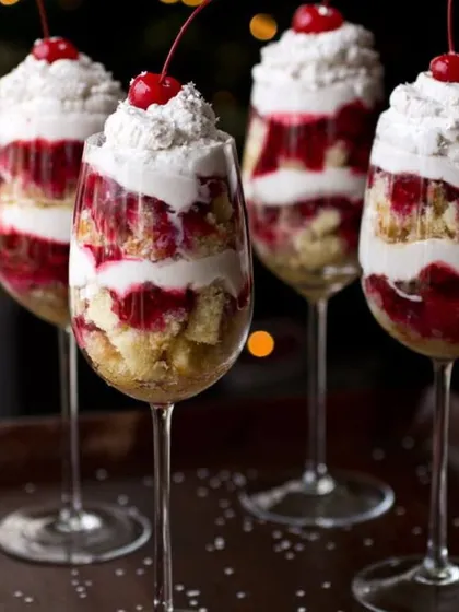 These are my layered dessert trifles, served elegantly in wine glasses. This one features layers of soft eggless cake, creamy white frosting, and a tangy cherry compote, all topped with a fresh cherry. It's a perfect dessert for a special dinner.