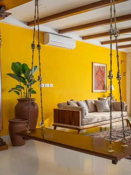 In our 'Vasudhalayah' project, we created a warm, ethnic living room centered around a traditional wooden swing and antique Chettinad pillars. The vibrant yellow accent wall and custom teak furniture create an inviting space for family gatherings.