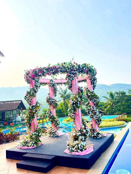 A vibrant pink floral mandap set against a stunning poolside and mountain view. The structure is wrapped in pink fabric and adorned with spiraling garlands of flowers, creating a cheerful and picturesque setting for a destination wedding.