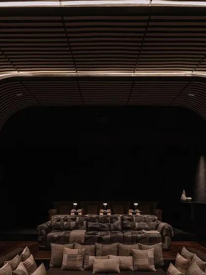 A glimpse into the dedicated home theatre at Rehethaan. We designed the space with curved, slatted walls and plush, tiered seating to create an immersive and luxurious cinematic experience for the family.