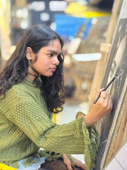 A student in our studio, fully immersed in her work on a conceptual charcoal portrait, demonstrating the focus and passion we see in our artists.
