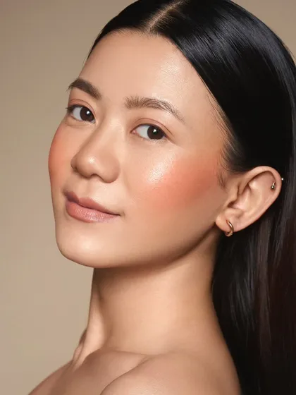 This image demonstrates how a peachy blush can warm up the complexion for a fresh, youthful look. The skin is kept dewy and the hair is sleek and simple.