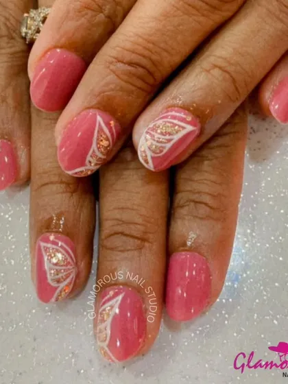 A soft and pretty manicure with pink nails and accent nails featuring a delicate butterfly wing design in white and gold glitter.