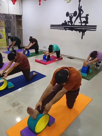 Students are using yoga wheels and blocks to deepen their hamstring stretch in this seated forward bend variation. The props provide support and allow for a more effective and accessible stretch.